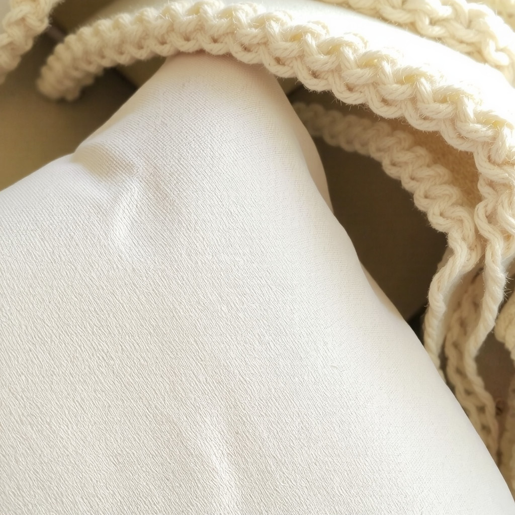 Close-up detail of a textured beige linen sofa cushion layered with a chunky knit wool throw in soft cream, highlighting natural fabric weaves.