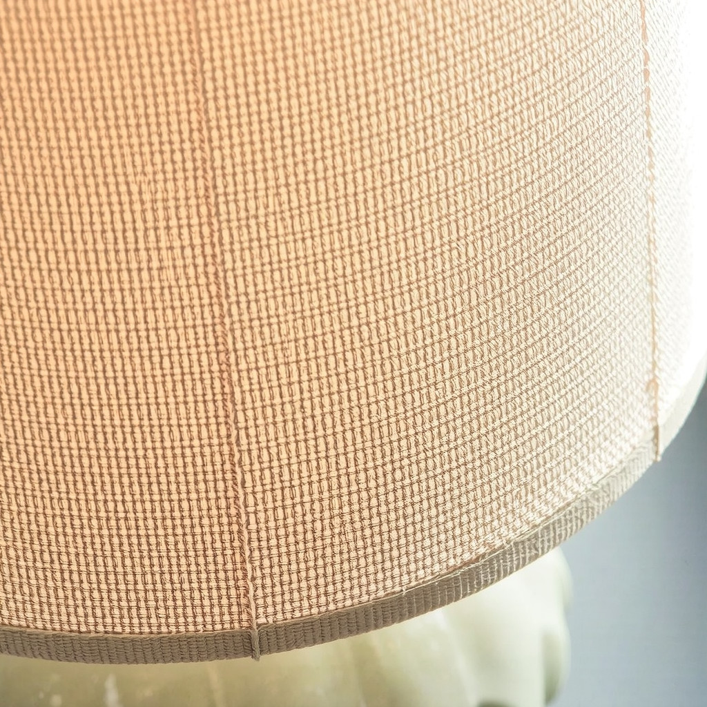 A close-up detail shot of a textured oatmeal linen lampshade on a ceramic base showing the weave of the fabric